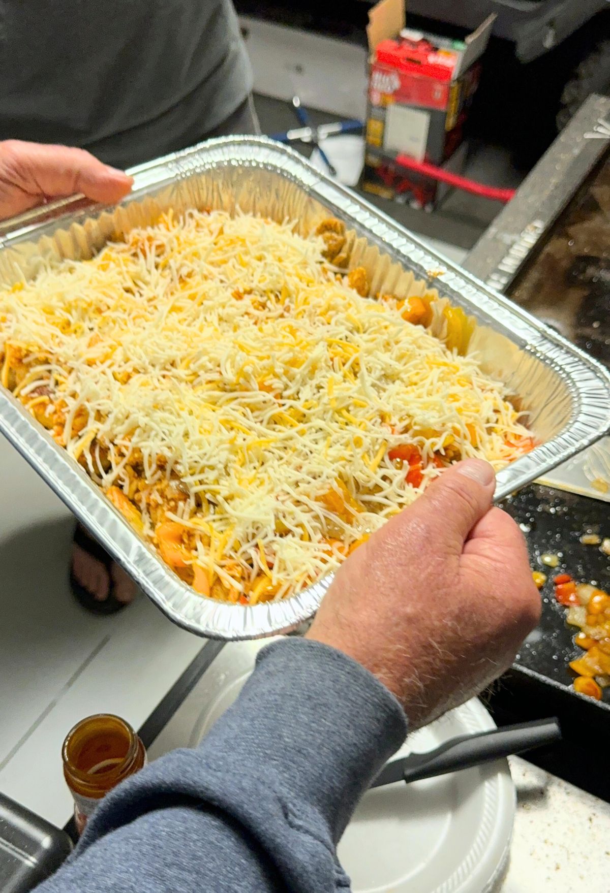A person holding a tray of pasta topped with shredded cheese, ready to be baked.