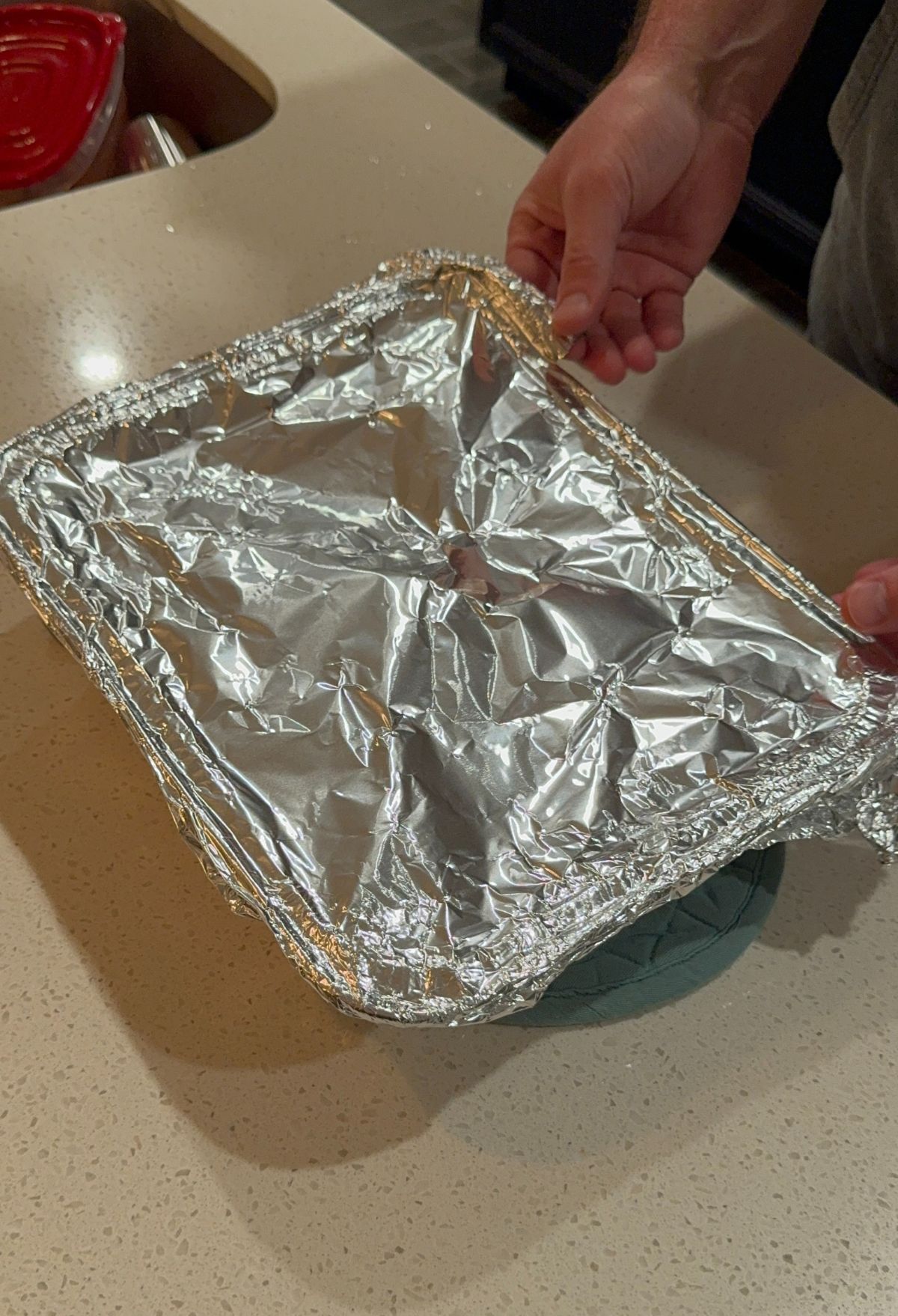 A person's hands holding a foil-covered tray over a kitchen counter.
