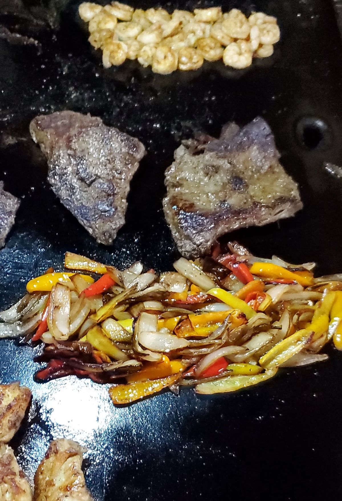 Sauteed vegetables and slices of beef on a black frying pan.